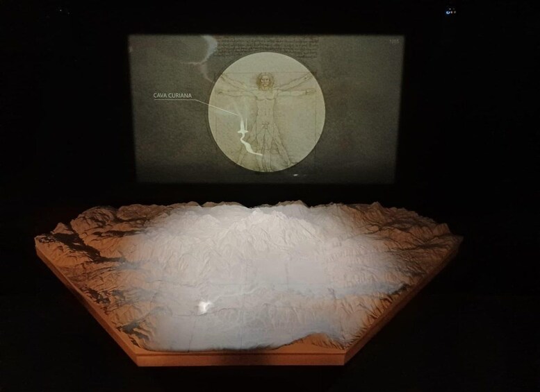 A sculpture of a figure with a halo, labeled 'CAVA CURIANA,' placed on a wooden base with a textured surface. 4