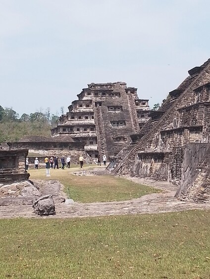 An ancient stone structure with multiple levels and a group of people walking around it. 5