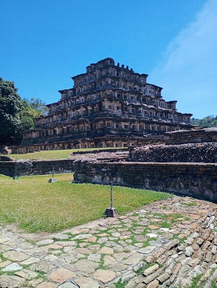 A large, multi-tiered stone structure with a grassy foreground and a clear blue sky. 2