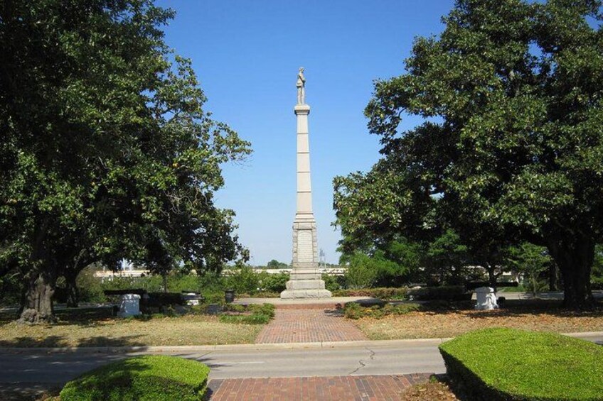 A tall monument with a statue on top, surrounded by trees and a paved walkway. 2