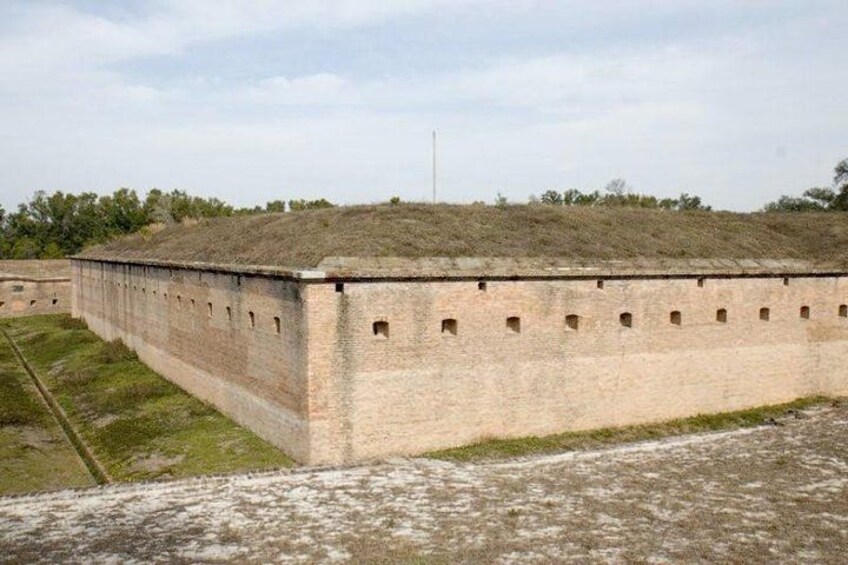 A large brick structure with a flat roof, surrounded by grassy terrain and trees. 1