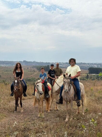 A group of people riding horses on a grassy hill with a cityscape in the background. 1