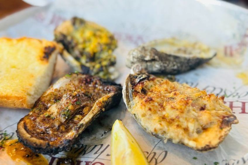 A plate of food with grilled oysters, a slice of bread, and a lemon wedge. 1