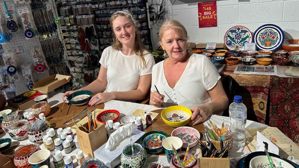 Two women at a craft table with bowls, paint bottles, and paintbrushes. 3