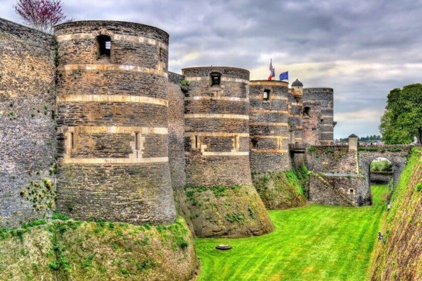 A medieval castle with multiple round towers, a grassy foreground, and a cloudy sky. 5