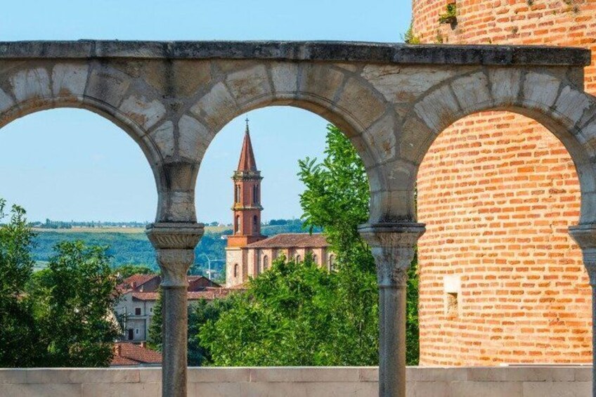 A stone archway with a brick tower and a church in the background. 3