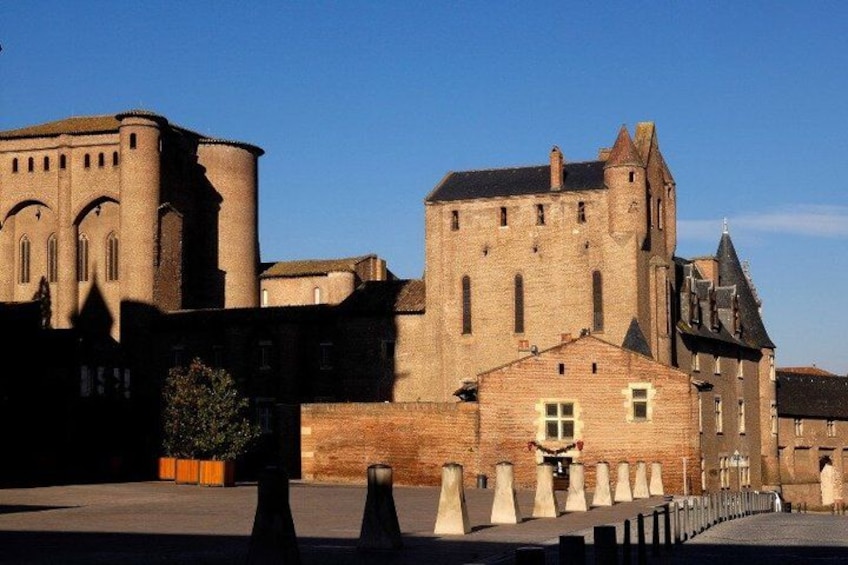 A historic stone building with a tower and arched windows, surrounded by a low wall and bollards. 5