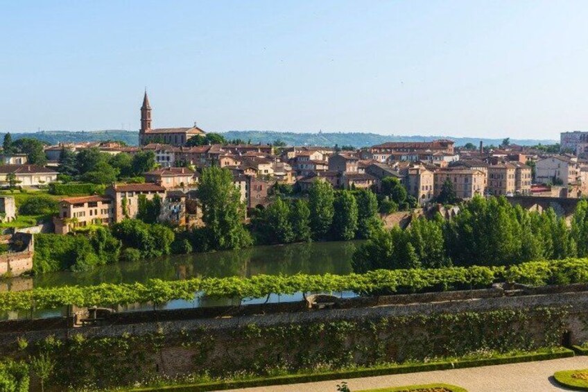 A riverside town with historic buildings, a prominent tower, and lush greenery. 2