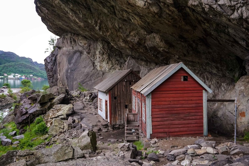 Une petite construction en bois avec une porte rouge, située sur un terrain rocheux près d’une falaise et d’une étendue d’eau. 3