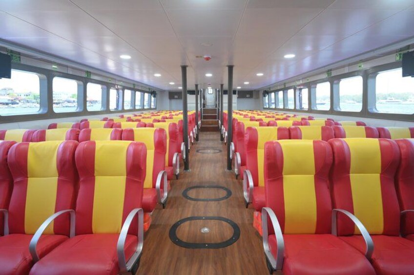 A train interior with rows of red and yellow seats, wooden flooring, and large windows along the sides. 5