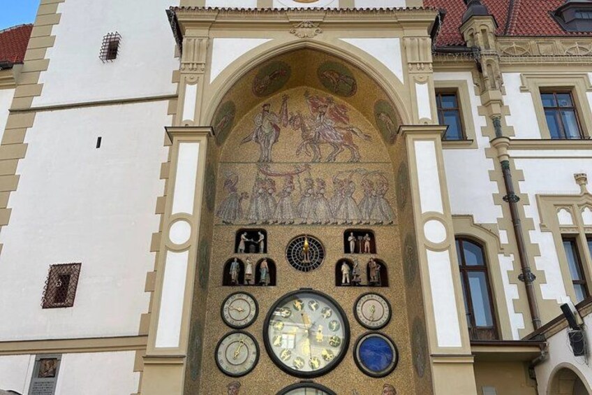 A building facade with a clock tower, a mural, and a series of clocks. 5