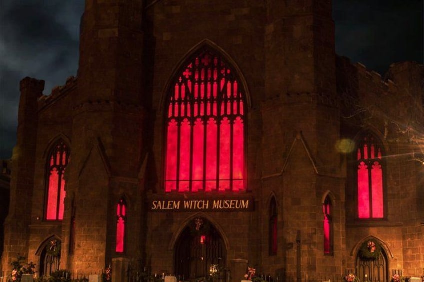 A historic building with arched windows and the text 'Salem Witch Museum' illuminated in red. 4