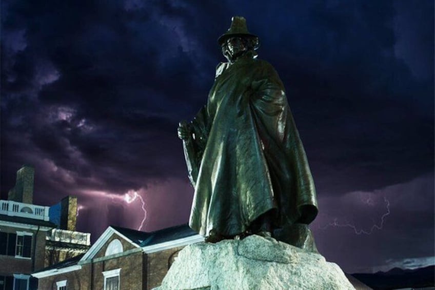A statue of a man in a long coat and hat, standing on a pedestal, with a stormy sky and lightning in the background. 3