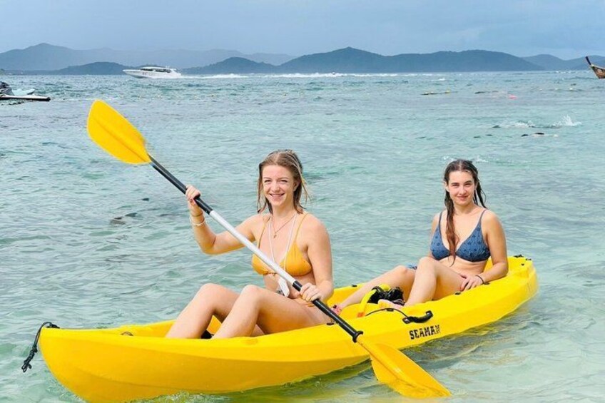 Two people in a yellow kayak on calm water with a boat in the background. 2