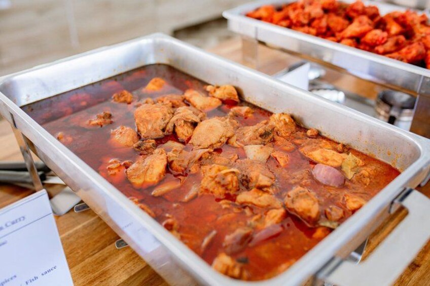 A buffet table with a dish of chicken in a red sauce. 5