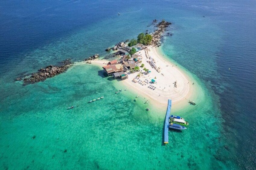 An aerial view of a tropical island with clear turquoise waters, a sandy beach, and a small settlement with buildings and boats. 4
