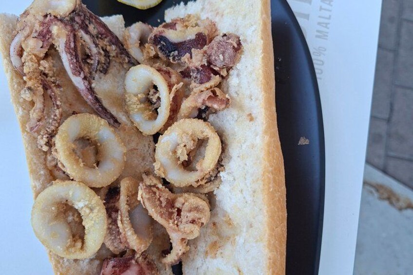 A sandwich with fried squid rings and meat on a white plate. 4