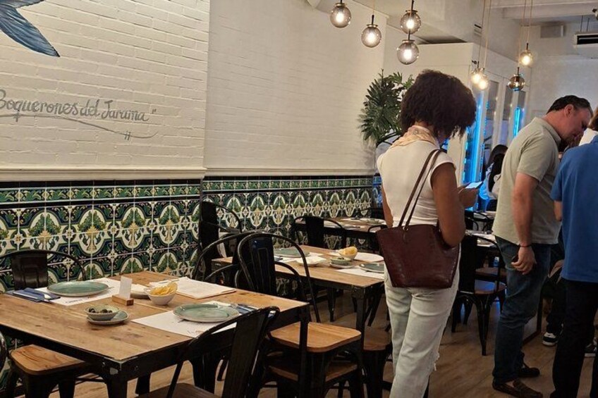 A restaurant interior with tiled walls, wooden tables, and hanging lights. 5