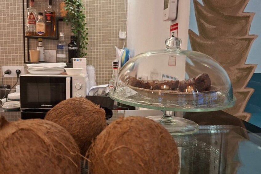 A kitchen counter with a glass dome displaying chocolate-covered items, a microwave, and various kitchen appliances. 3