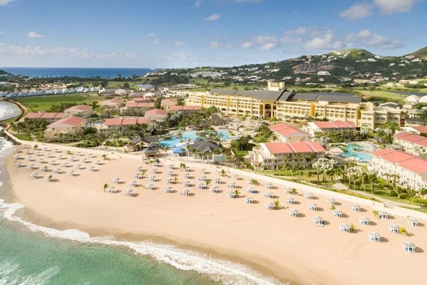 A beach resort with a large hotel, numerous beach umbrellas, and a clear view of the ocean. 1