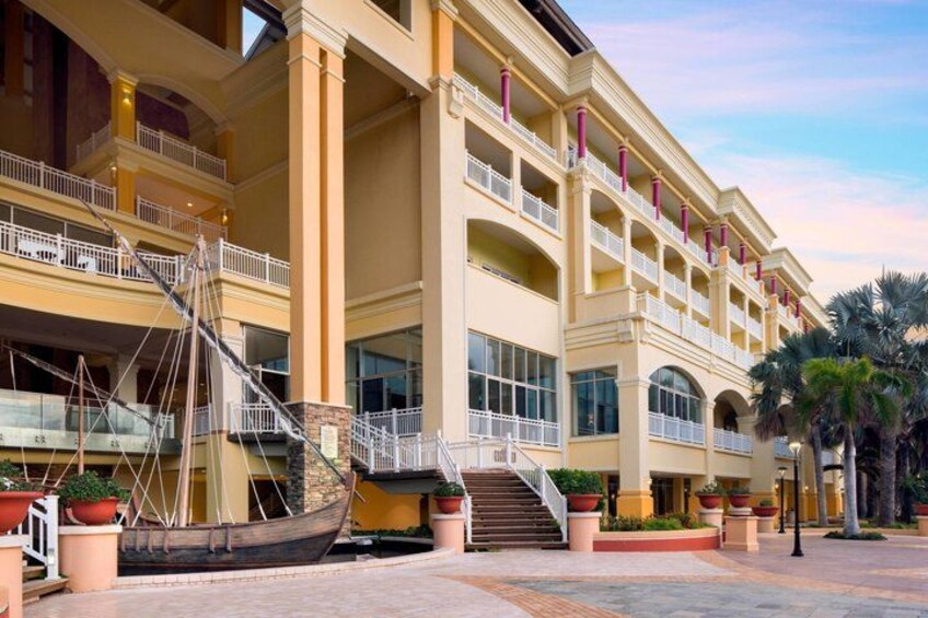 A multi-story hotel with balconies, palm trees, and a boat in the foreground. 3