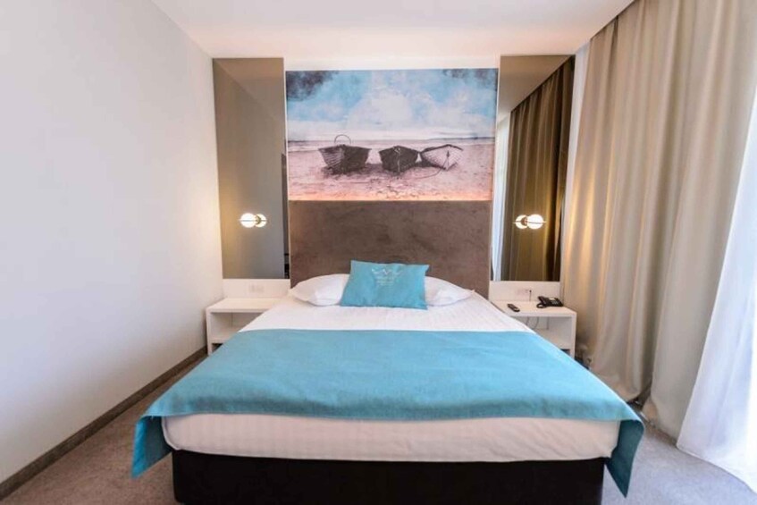 Habitación de hotel con una cama, un cuadro de barcos en la pared y vista al mar. 4