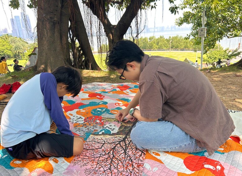 Twee personen zitten op een kleurrijke deken buiten, met een boom en een park op de achtergrond. 4