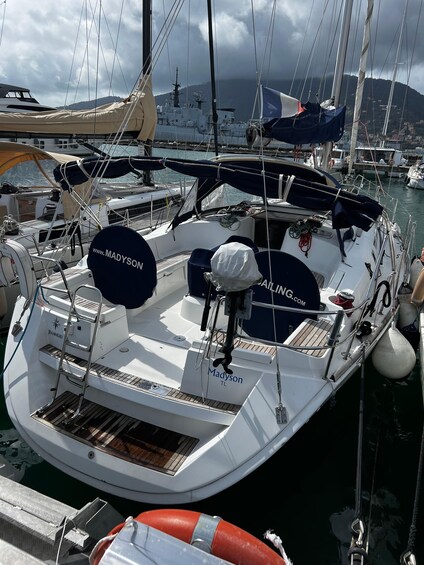 Eine weiße Yacht liegt in einer Marina, umgeben von anderen Booten, einem Rettungsring und einem bewölkten Himmel. 3