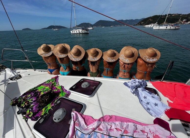 Ein Boot mit mehreren Personen, die Hüte und Badesachen tragen, einem bunten Handtuch und einem roten Sonnenschirm auf dem Deck. 1