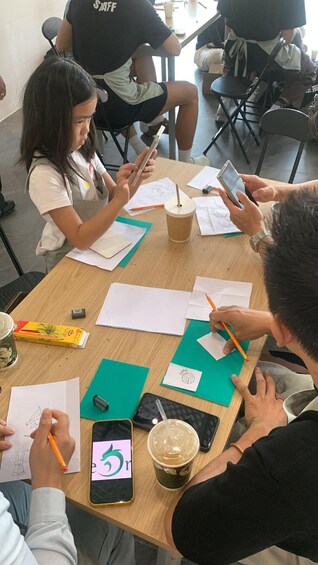 Un groupe de personnes est assis autour d’une table, devant des feuilles de papier, des crayons et un téléphone intelligent. 3