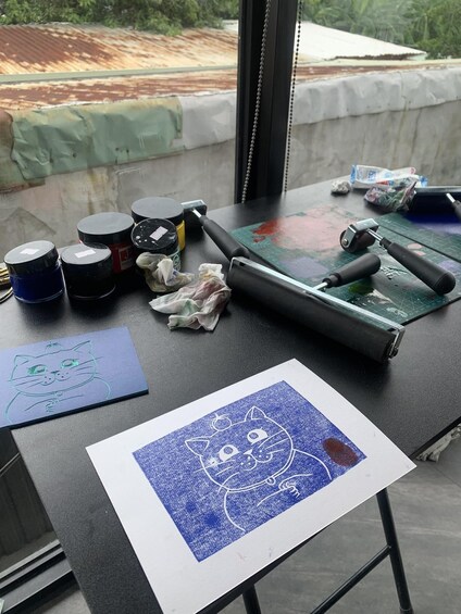 Un espace de travail équipé de matériel de dessin, d’un tapis enroulable et où l’on peut voir deux œuvres d’art. 1