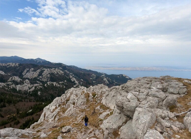 A hiker on a rocky mountain ridge with a view of distant mountains and a body of water. 4