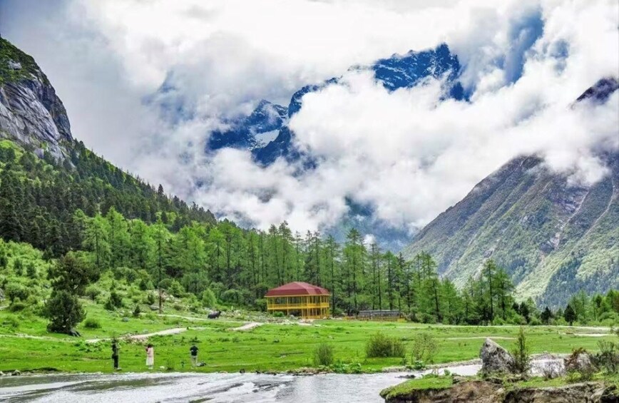 A mountainous landscape with a river, a small building, and a forested area. 3