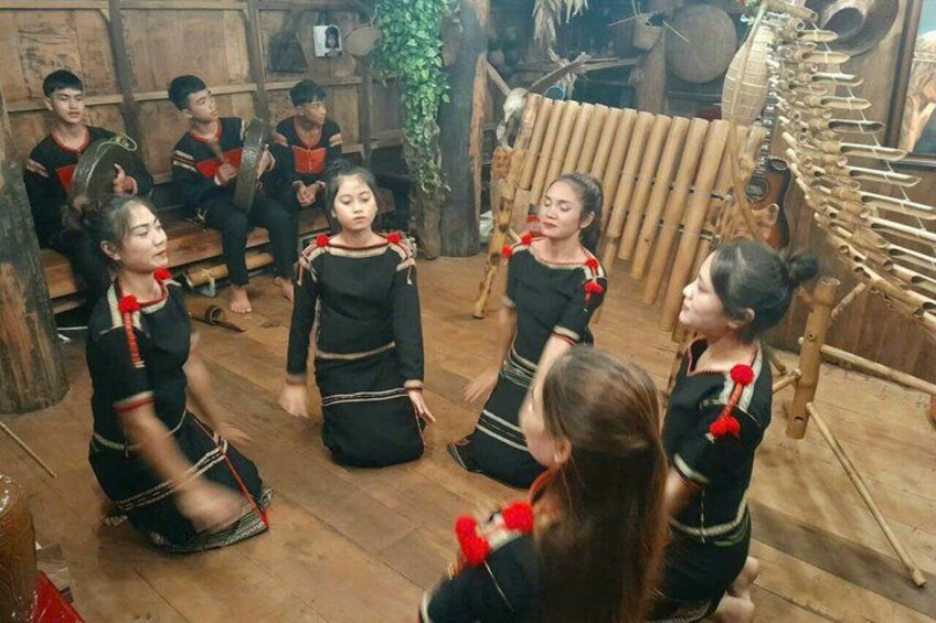 Un grupo de personas con vestimenta tradicional bailando en un entorno rústico con paredes de madera y una estructura de bambú. 5