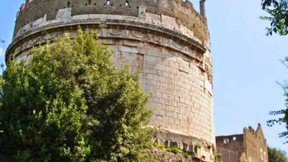 Ein historischer Steinturm mit runder Basis und Zinnen, umgeben von viel Grün. 3