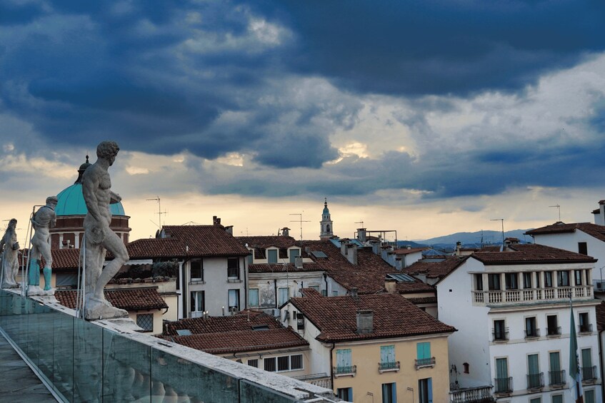 A cityscape with a prominent statue on a bridge, historic buildings, and a cloudy sky. 2