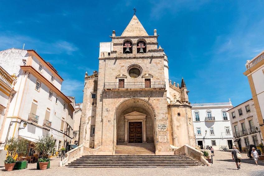 A historic stone church with a bell tower, a large arched entrance, and a staircase leading up to it. 1