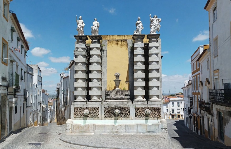 A street with a central monument featuring statues and a fountain. 4
