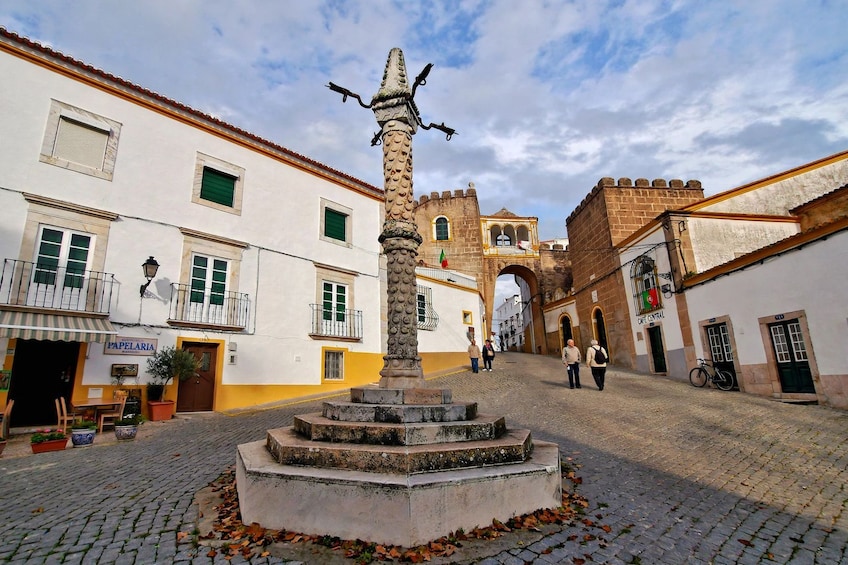 A cobblestone street with a central fountain, historic buildings, and a castle-like structure in the background. 5