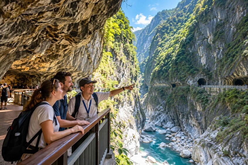 A group of tourists on a wooden observation deck overlooking a river canyon with steep cliffs and a bridge. 1