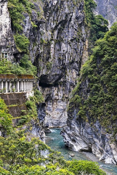 A river flowing through a rocky gorge with lush greenery and a structure with columns on the left. 3