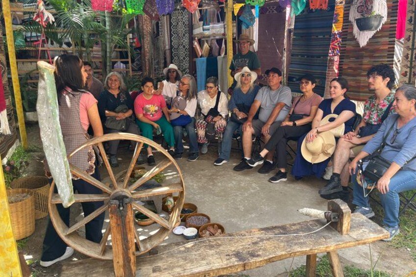 A group of people sitting around a wooden wheel and bench in a rustic outdoor setting. 2