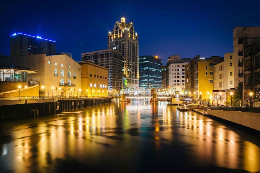A nighttime cityscape with a river reflecting lights, a prominent building with a tower, and various other illuminated buildings along the riverbanks. 3