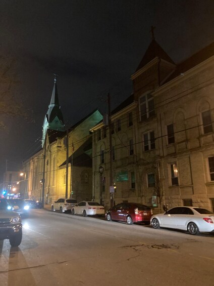 A nighttime street scene with cars parked along the side and a building with a green-lit entrance. 5