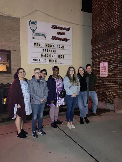 A group of people standing in front of a sign that reads 'Hosed on Brady St. Make Hosed Your Brewers Watching Spot Suck It Mike.' 2