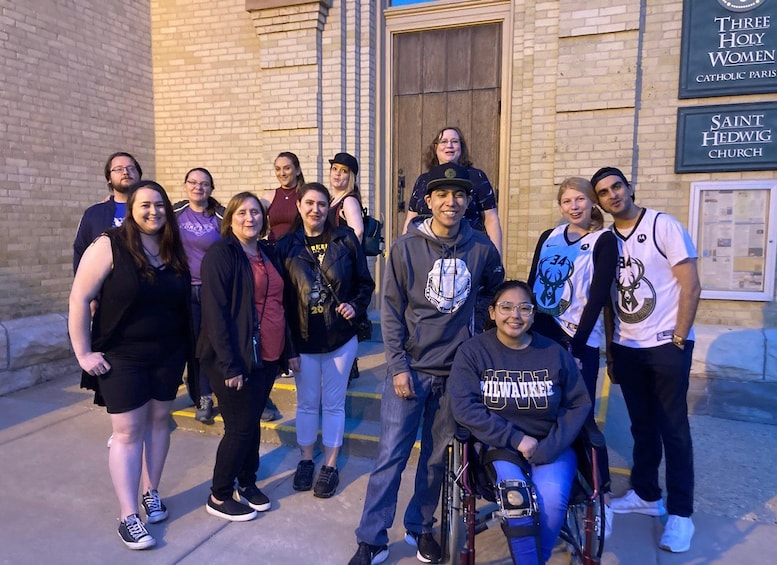 A group of people standing in front of a building with signs for 'Three Holy Women Catholic Parish' and 'Saint Hedwig Church.' 4