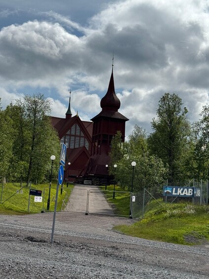 A church with a tall spire, a pathway leading to it, and a fence with a sign. 4