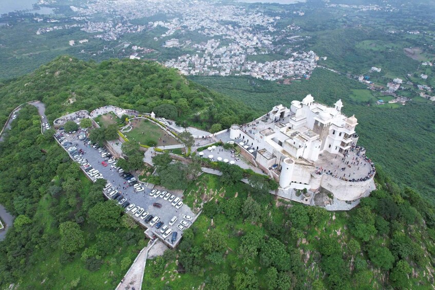 Une vue aérienne d’un vaste complexe de temples blancs, entouré de collines verdoyantes, avec un espace de stationnement et une route menant à l’entrée. 5
