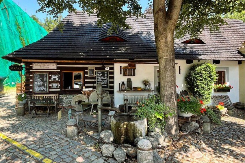 A rustic wooden building with a stone foundation, surrounded by a cobblestone path and a large tree. 4