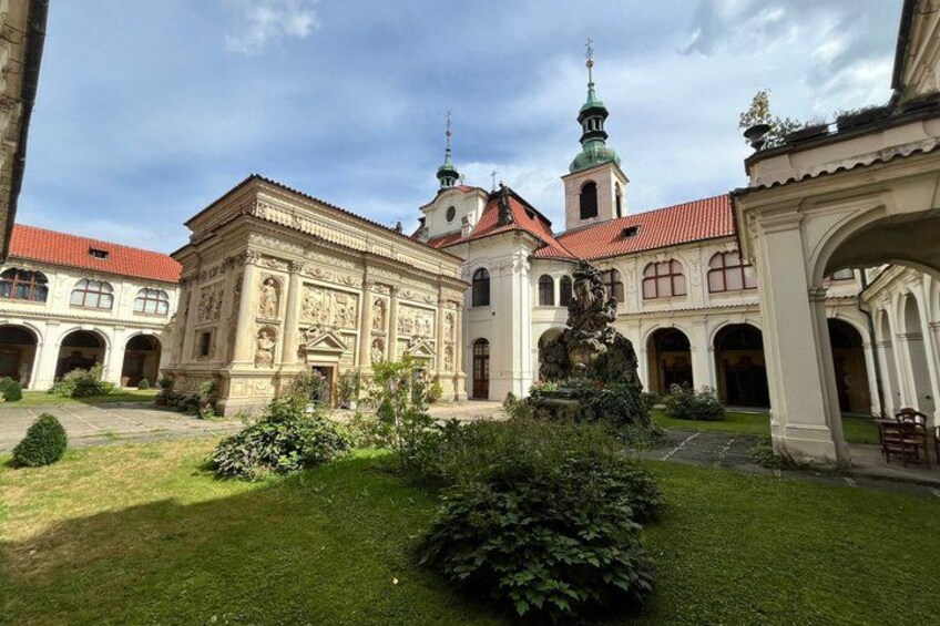 A courtyard with a fountain, a church with a green spire, and a building with intricate facade details. 2